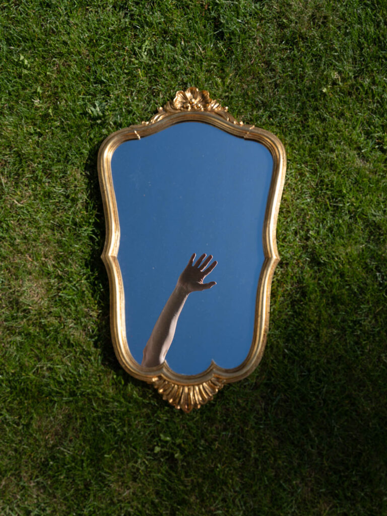 Cinematische Fotokunst einer Hand über einer Pfütze mit Himmelsspiegelung in einer Wiese, künstlerische Alltagsabstraktion von Richard Grando.